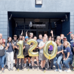 The Steinhauser team stands in front of the building with 120 balloons to celebrate the company's 120th anniversary in printing.