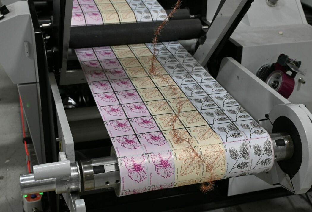 3 SKUs of a candle label running on the hybrid mark andy press. From left to right, pink, yellow, and blue.