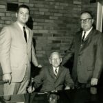 3 generations of Steinhauser ownership, Bobby and Wilbur Steinhauser stand on either side of Albert Steinhauser who is sitting down at a desk