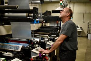 Press Operator looks up at label printing on a flexographic printing press in the Steinhauser production area